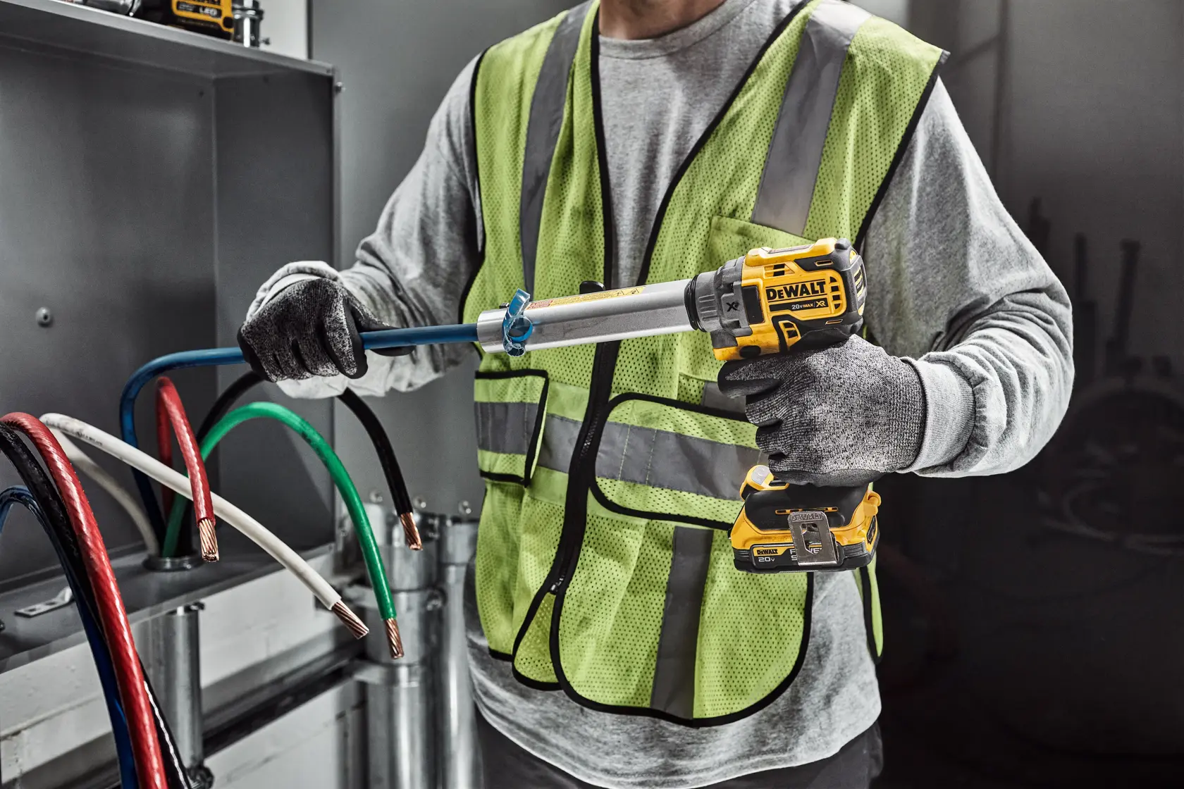 A worker wearing a safety vest and gloves uses a DEWALT DCE151B tool to cut or strip electrical cable in an industrial setting.