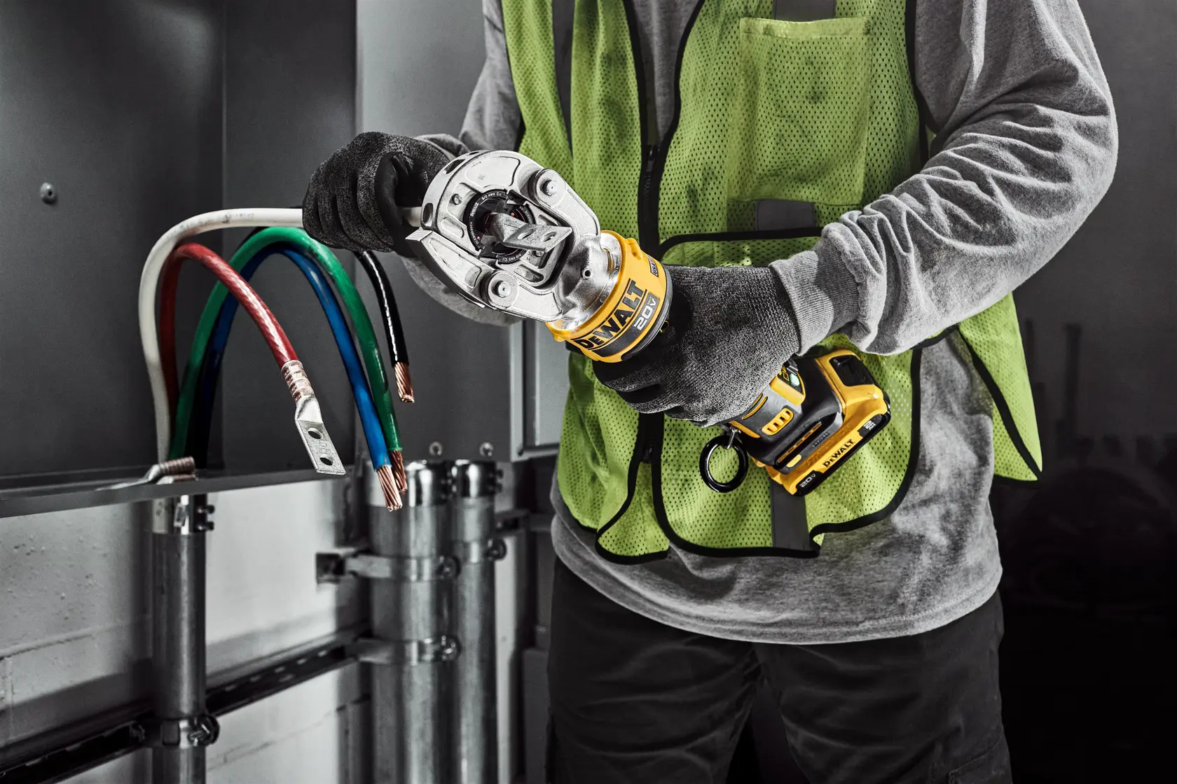 A person wearing a safety vest and gloves is using a DEWALT cordless cable crimping tool to crimp electrical cables inside an industrial setting.