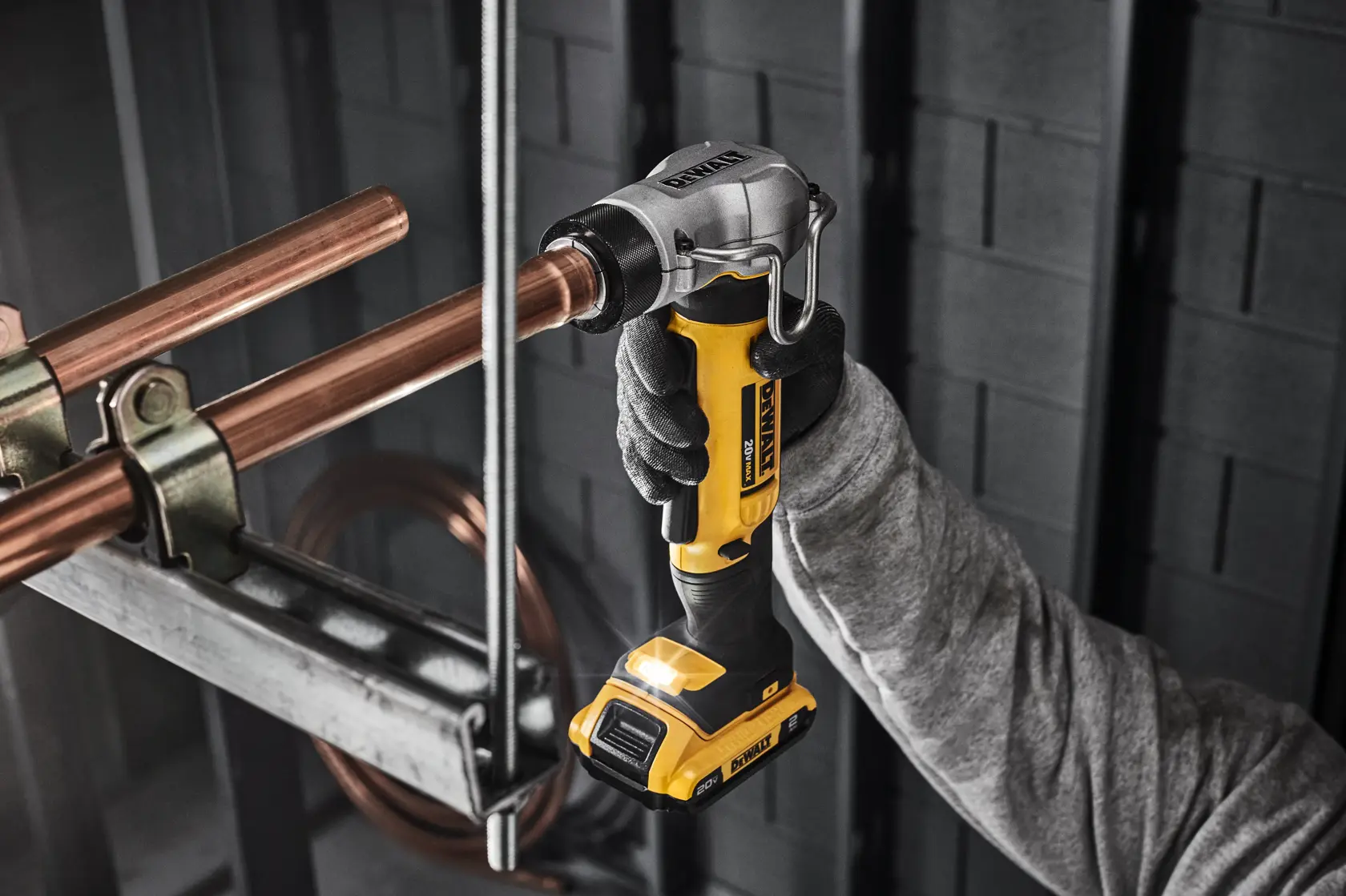 A person wearing gloves is using a yellow and black DEWALT cordless power tool to work on copper pipes in an industrial setting.
