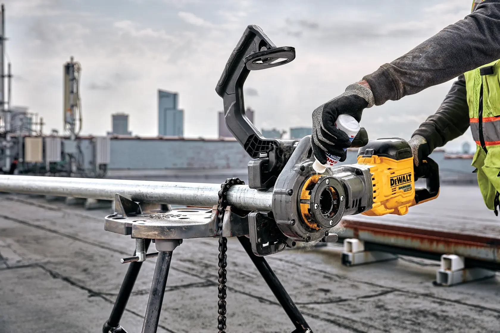 A worker uses a DEWALT electric pipe threader to thread a metal pipe secured on a tripod stand at an outdoor industrial site.
