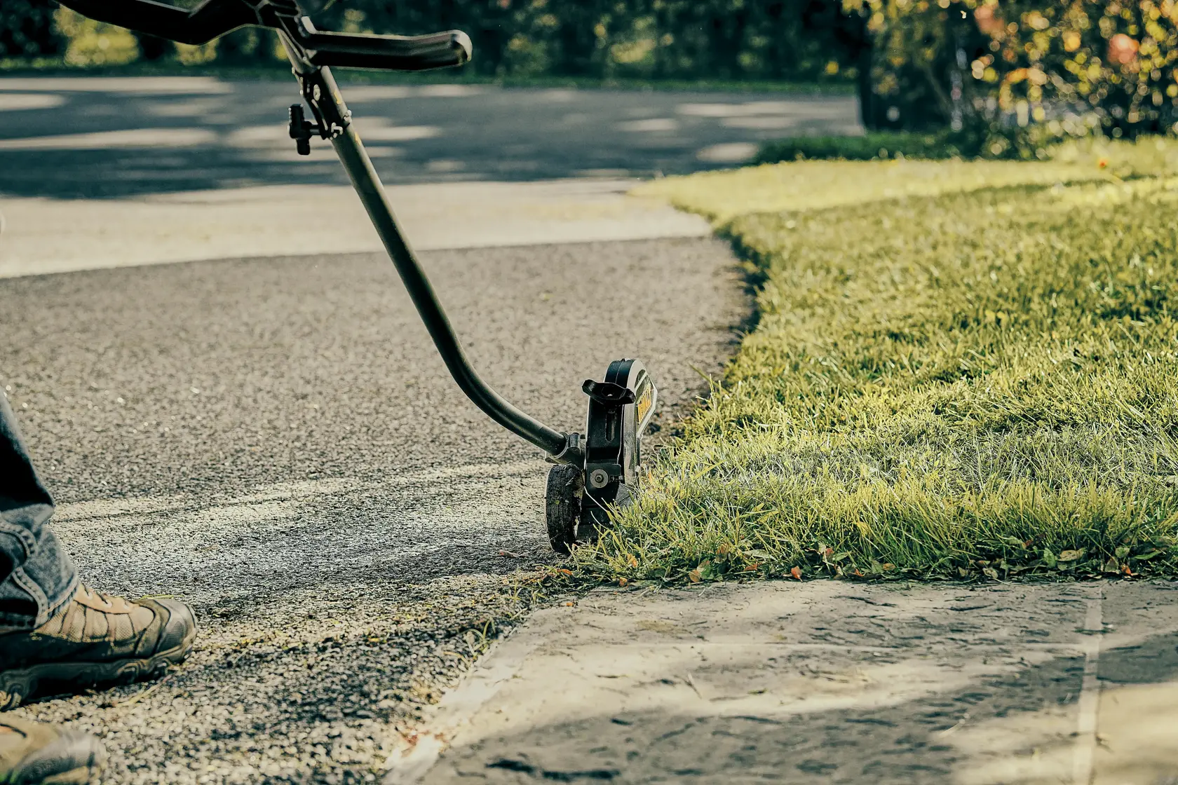 A close-up view of a DEWALT lawn edger trimming the grass edge along a sidewalk and driveway.