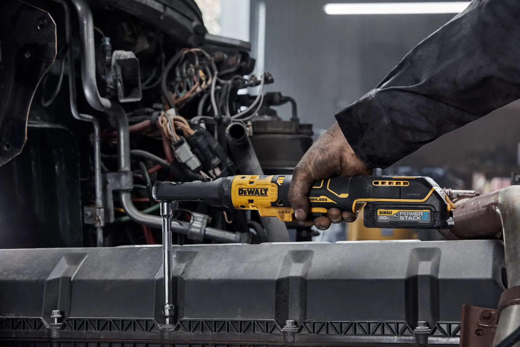A person using a DEWALT DCF510B cordless ratchet wrench to tighten a bolt inside an engine bay, with visible mechanical components and wiring.