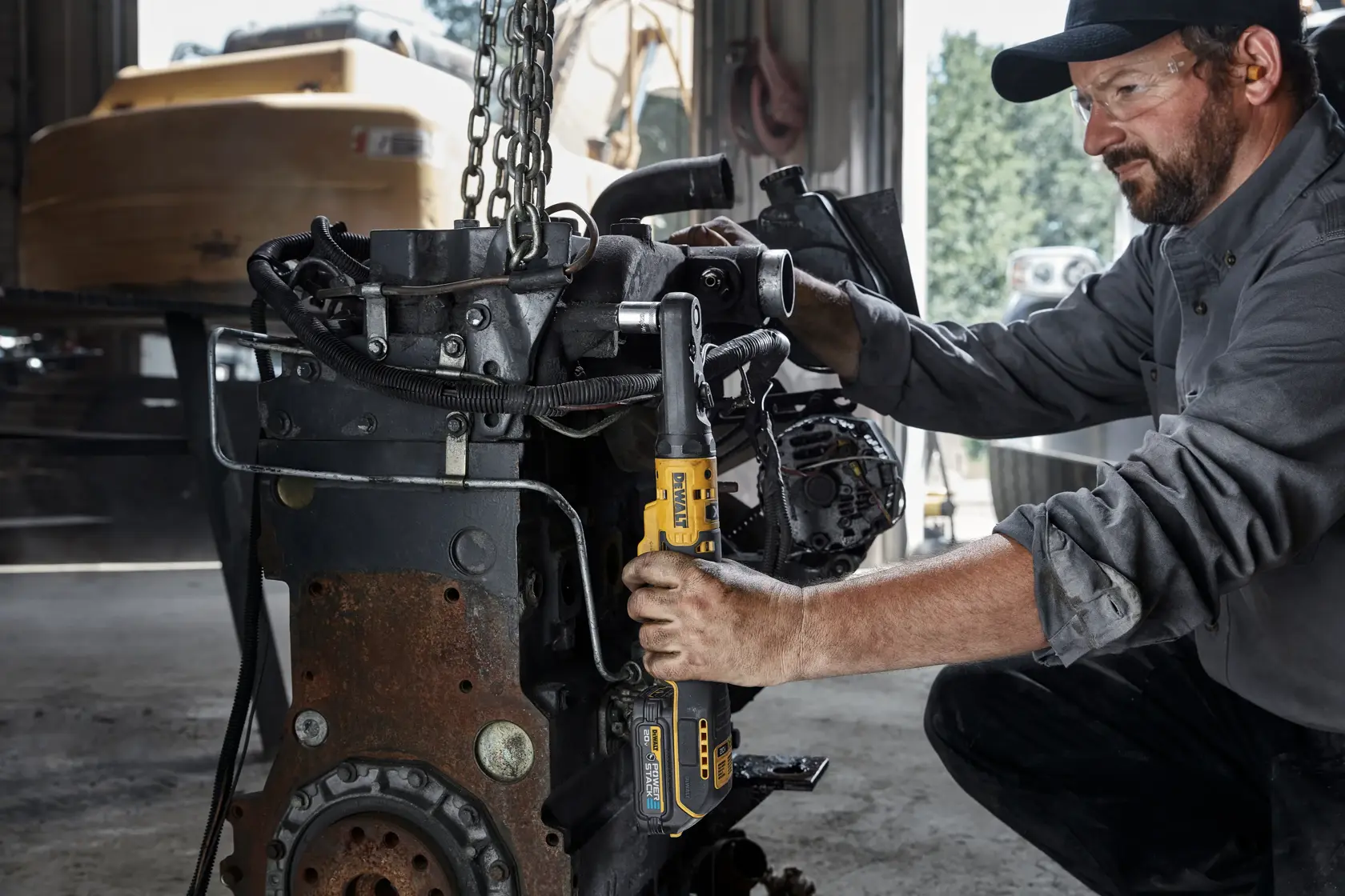 A person using a DEWALT DCF510B cordless ratchet tool to work on a rusty engine in a workshop. The person's face is blurred for privacy.