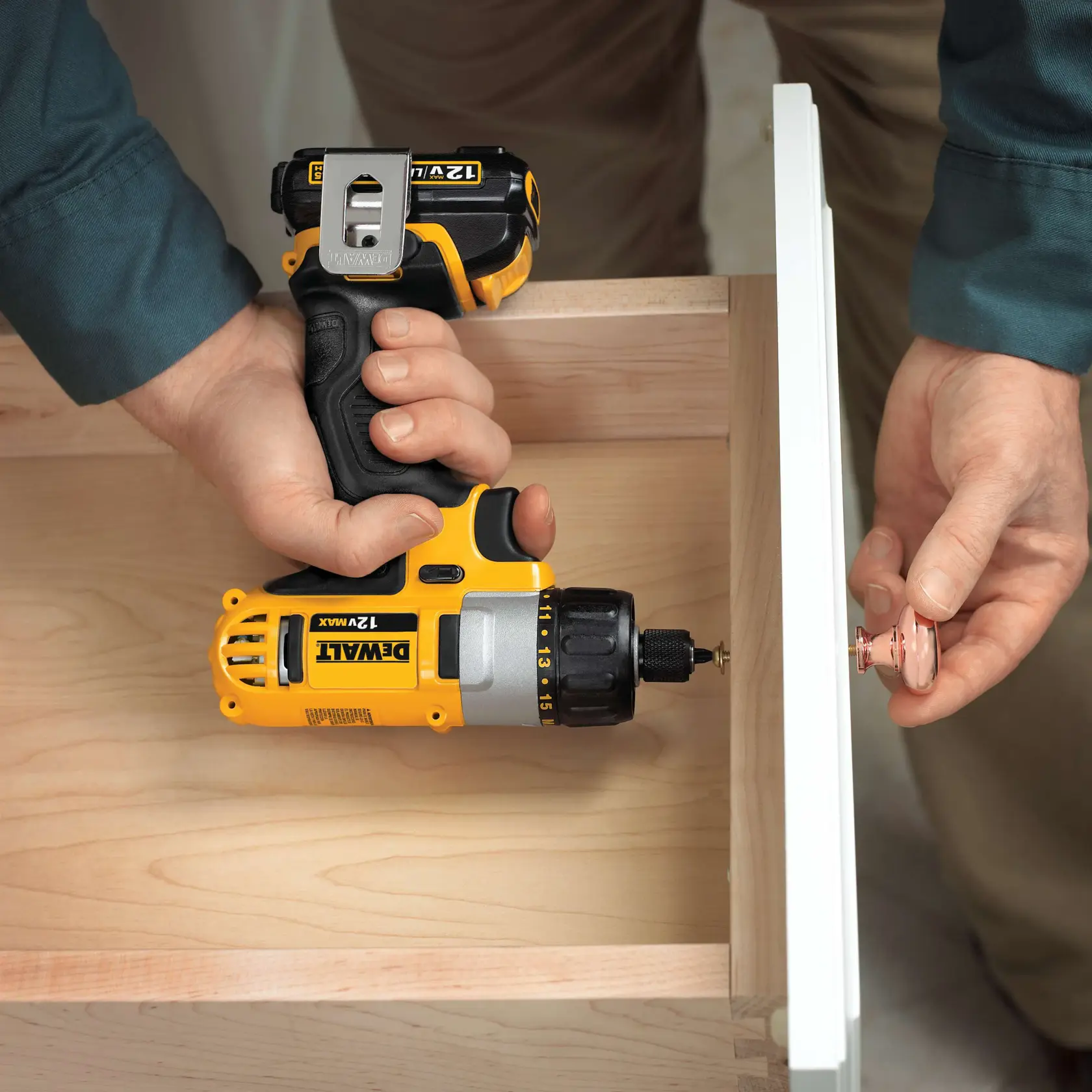 A person using a DEWALT 12V Max cordless drill to install a knob on a wooden drawer.
