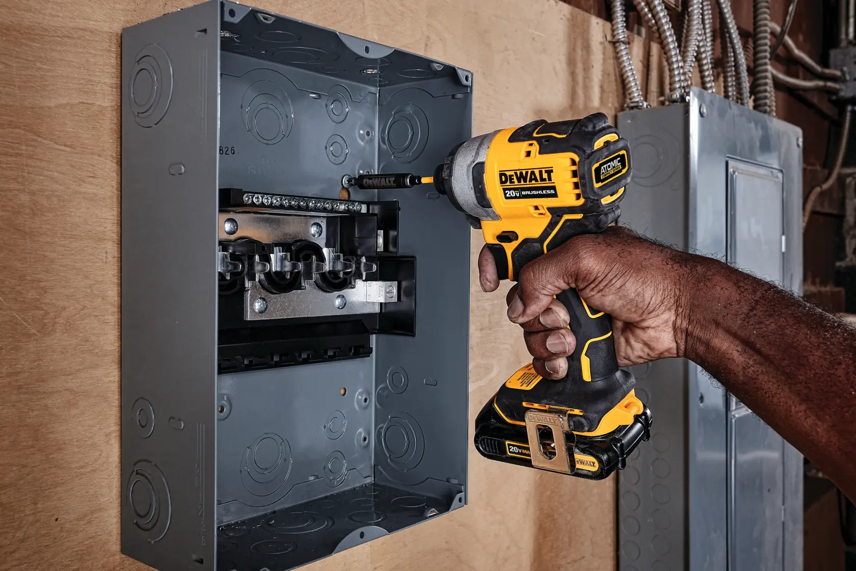 A person using a DEWALT cordless impact driver (model DCF809B) to work inside an electrical panel mounted on a wall.