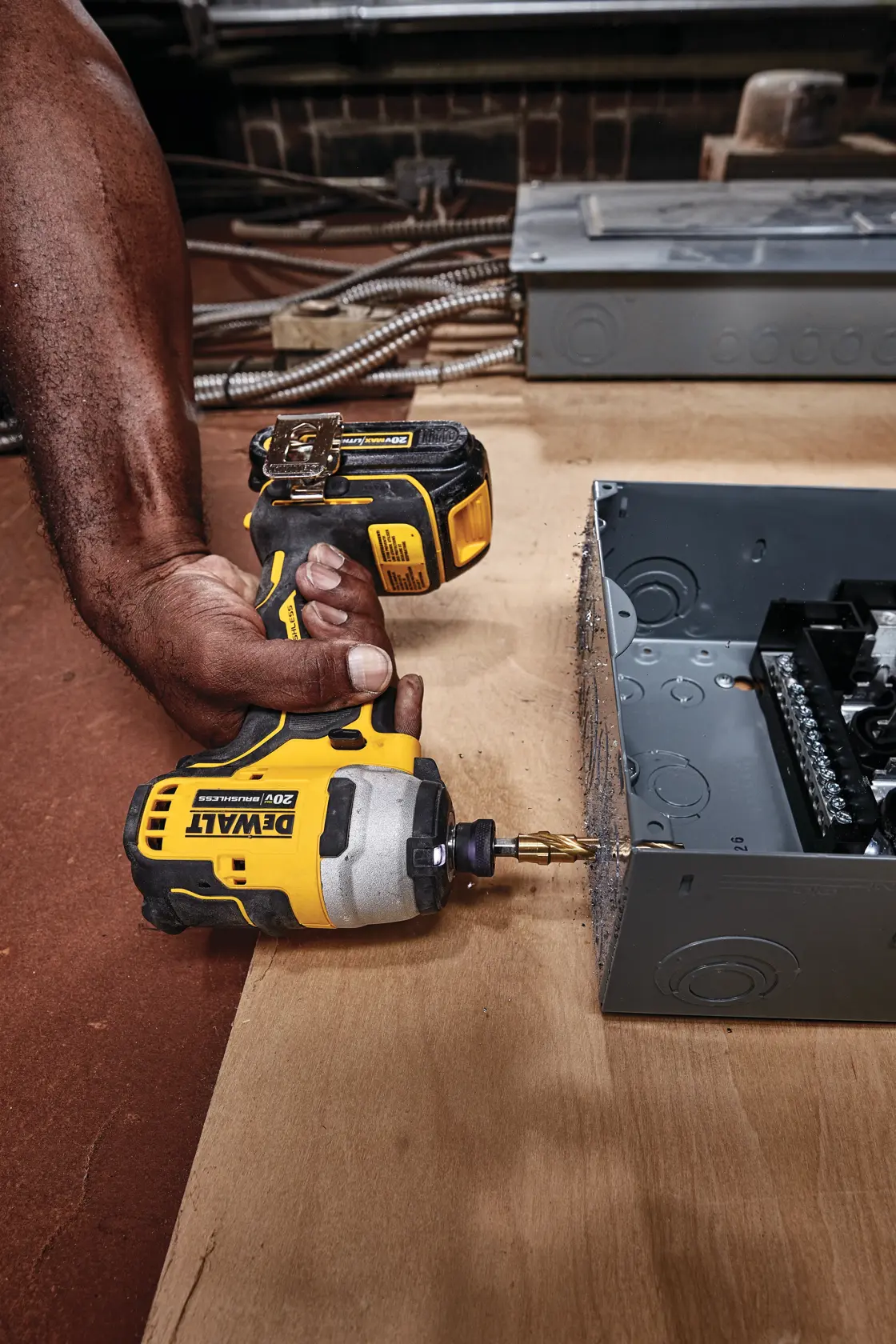 A person is using a DEWALT DCF809B 20V cordless impact driver to drill into a metal electrical box on a wooden surface.