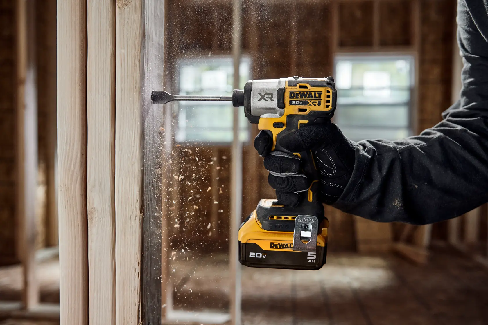 A DEWALT 20V XR cordless impact driver, model DCF845P1, being used to drill into a wooden beam at a construction site. Sawdust is flying as the tool operates, and the user is wearing black work gloves.