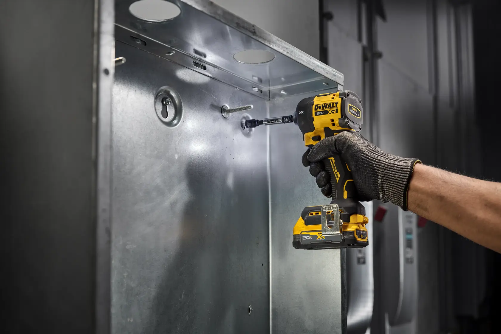 A person wearing a work glove uses a DEWALT DCF870B 20V cordless impact driver to fasten a screw into a metal electrical box.