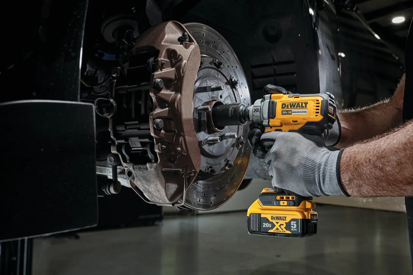 A person using a DEWALT 20V cordless impact wrench to work on the lug nuts of a car's wheel, with the tool held against the black rim.