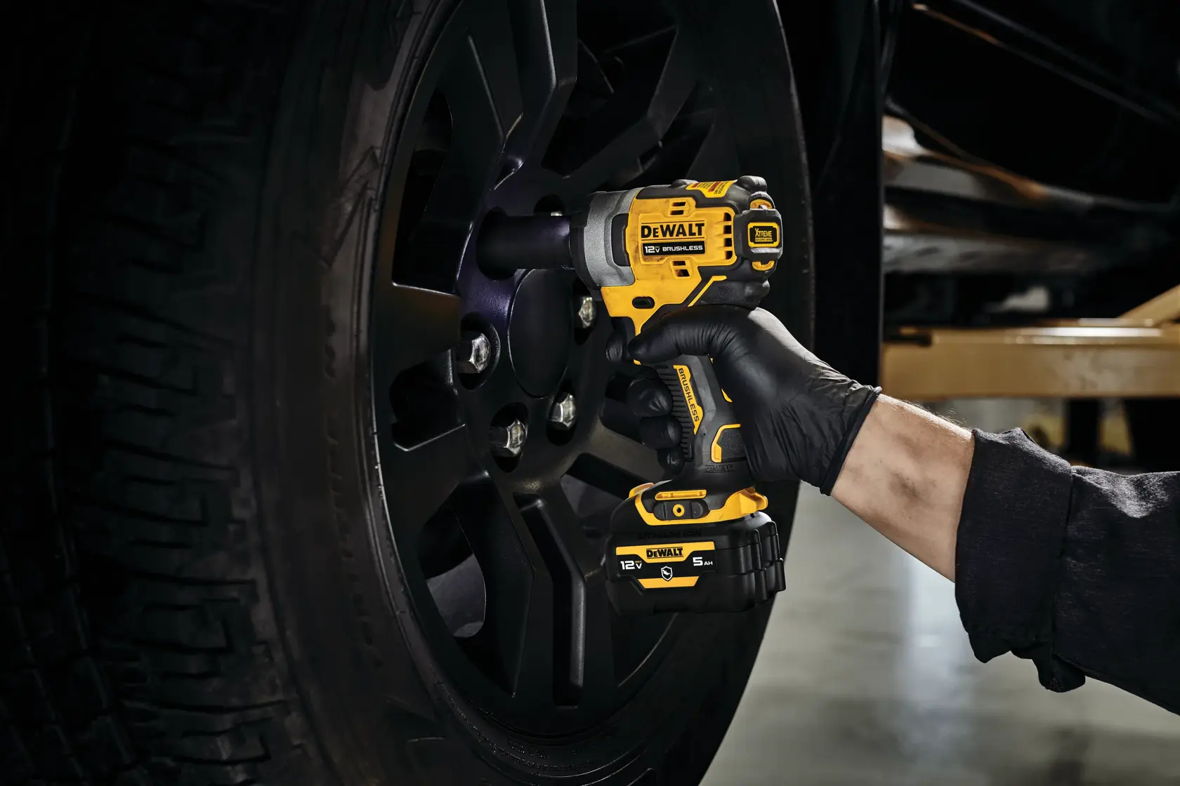 A person uses a DEWALT cordless impact wrench to tighten lug nuts on a black vehicle wheel.