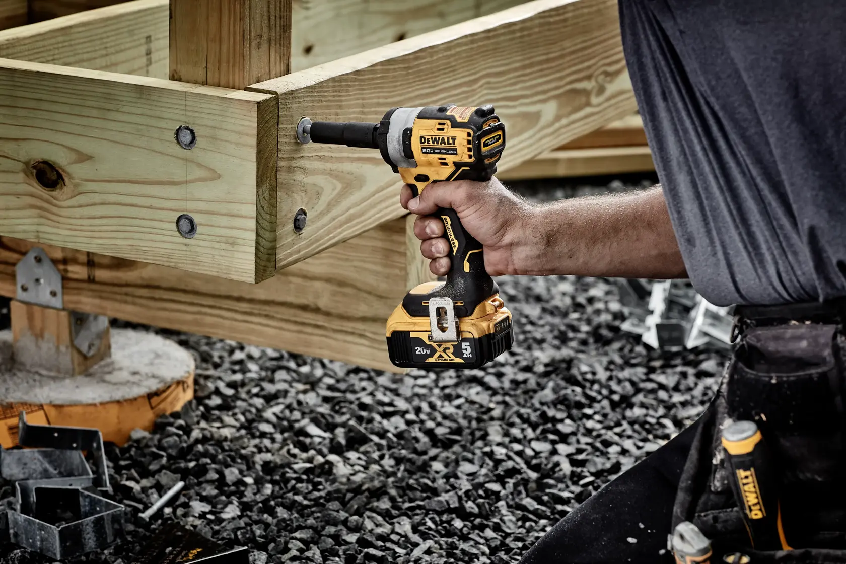 A person using a DEWALT DCF911B cordless impact wrench to fasten bolts on a wooden construction outdoors. The tool is yellow and black, powered by a 20V MAX XR battery.