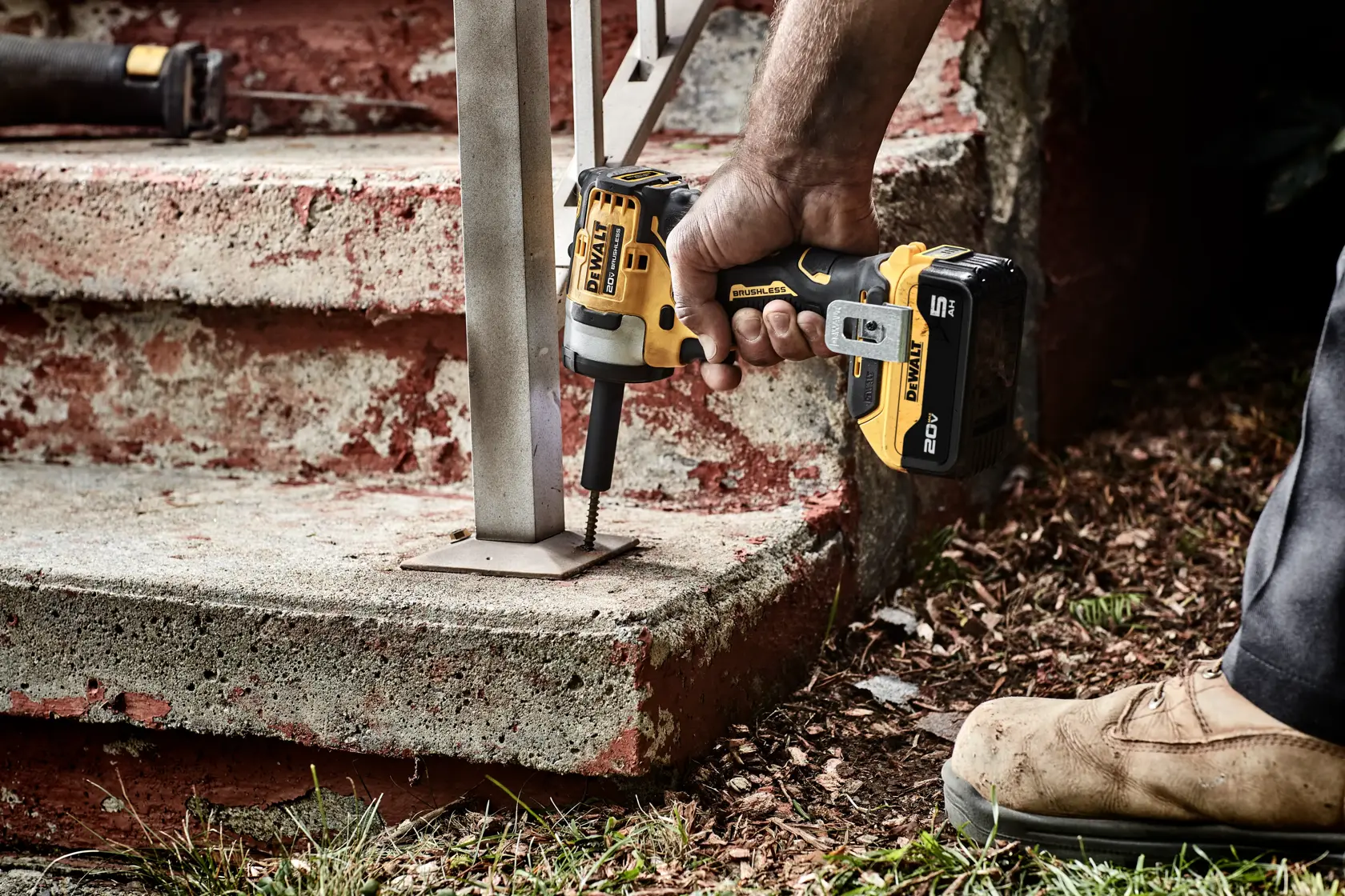 A person using a DEWALT 20V cordless impact wrench to secure a metal railing to concrete steps outdoors.