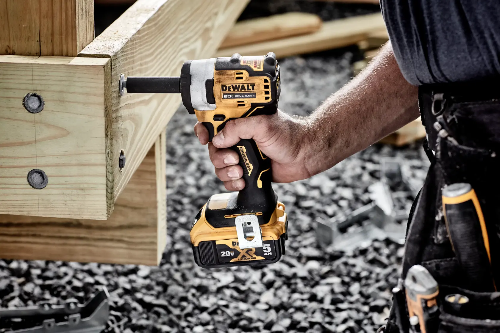 A person uses a DEWALT 20V cordless impact wrench to tighten a large bolt into a wooden structure, with tools visible on a tool belt.