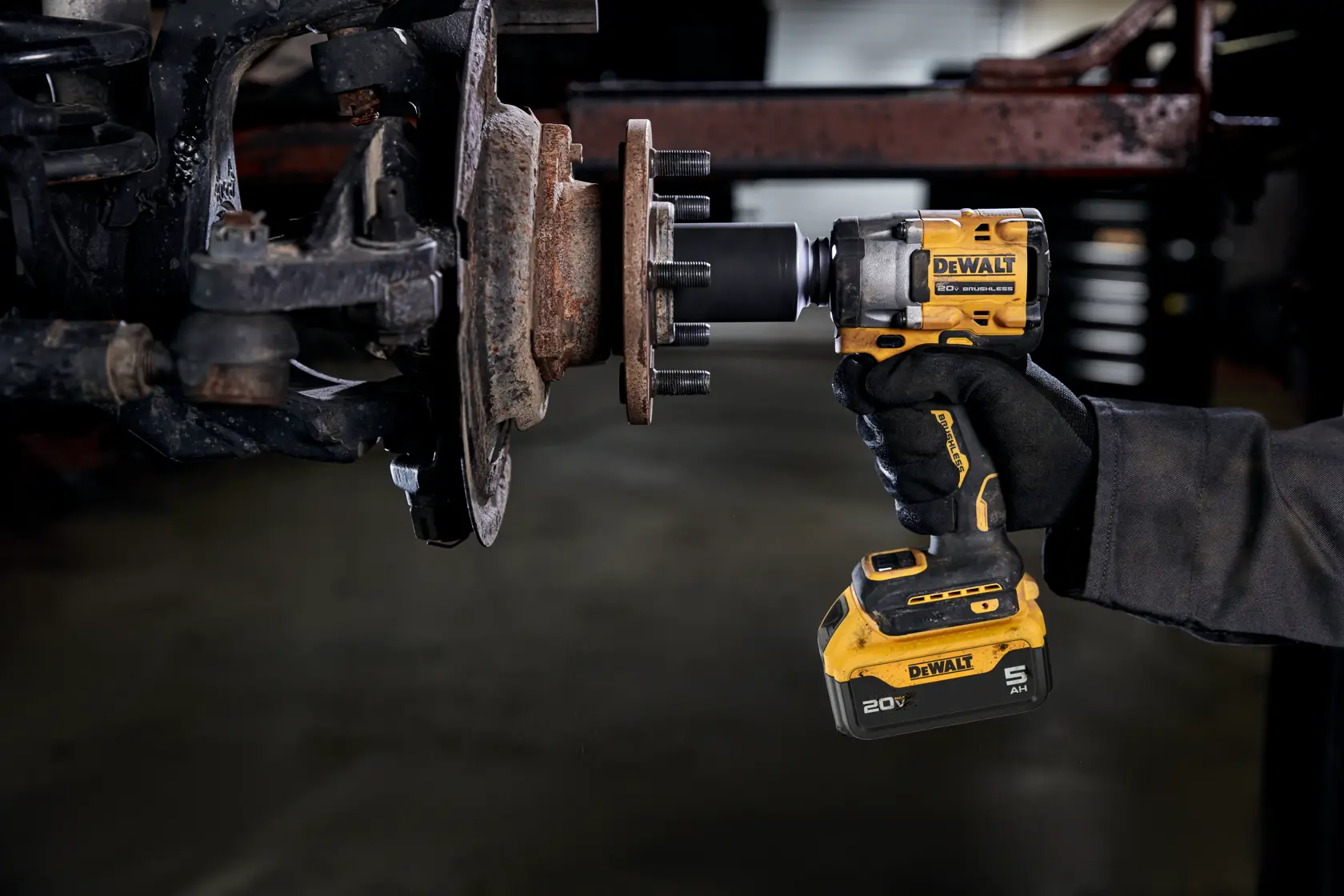 A person wearing gloves is using a DEWALT 20V MAX cordless impact wrench to work on the wheel hub assembly of a vehicle. The tool is yellow and black, and the wrench is being used to loosen or tighten bolts on the assembly.