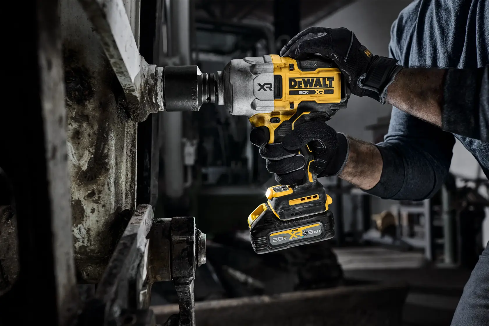 Gloved hands using a DEWALT cordless impact wrench on a large metal bolt in an industrial setting.