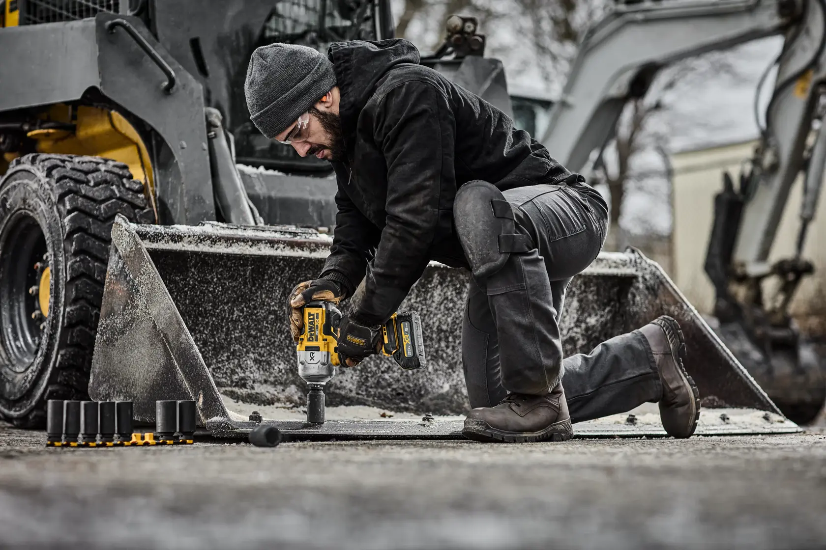 Person using a DEWALT impact wrench on construction equipment outdoors with sockets and machinery visible.
