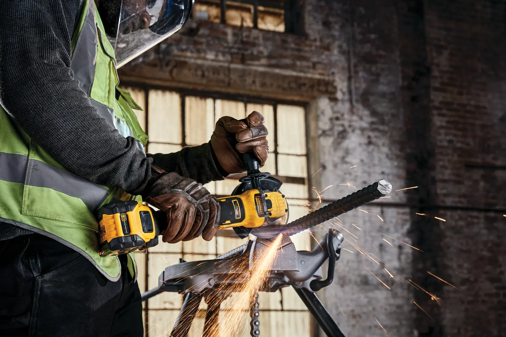 A person wearing safety gloves and a face shield uses a yellow DEWALT cordless angle grinder (model DCG416B) to cut through a metal rod, producing sparks in an industrial setting.