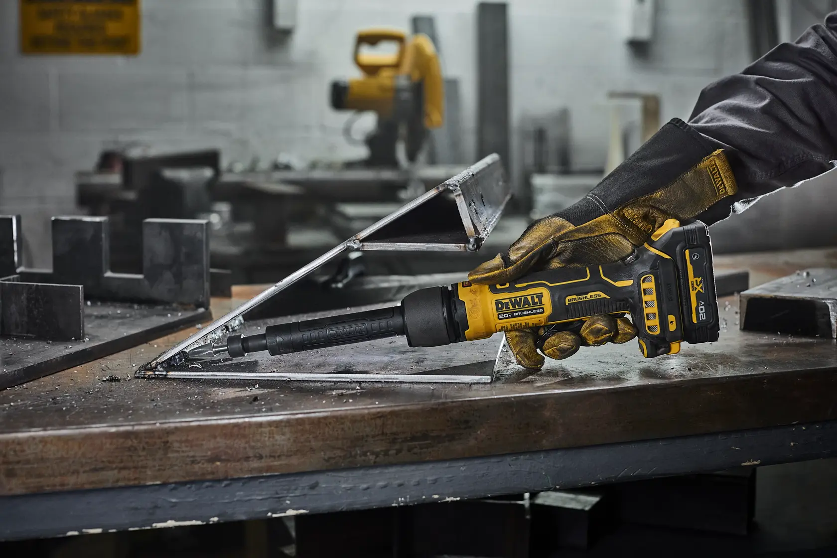 A person wearing work gloves uses a DEWALT cordless power tool to work on a metal structure in an industrial workshop.