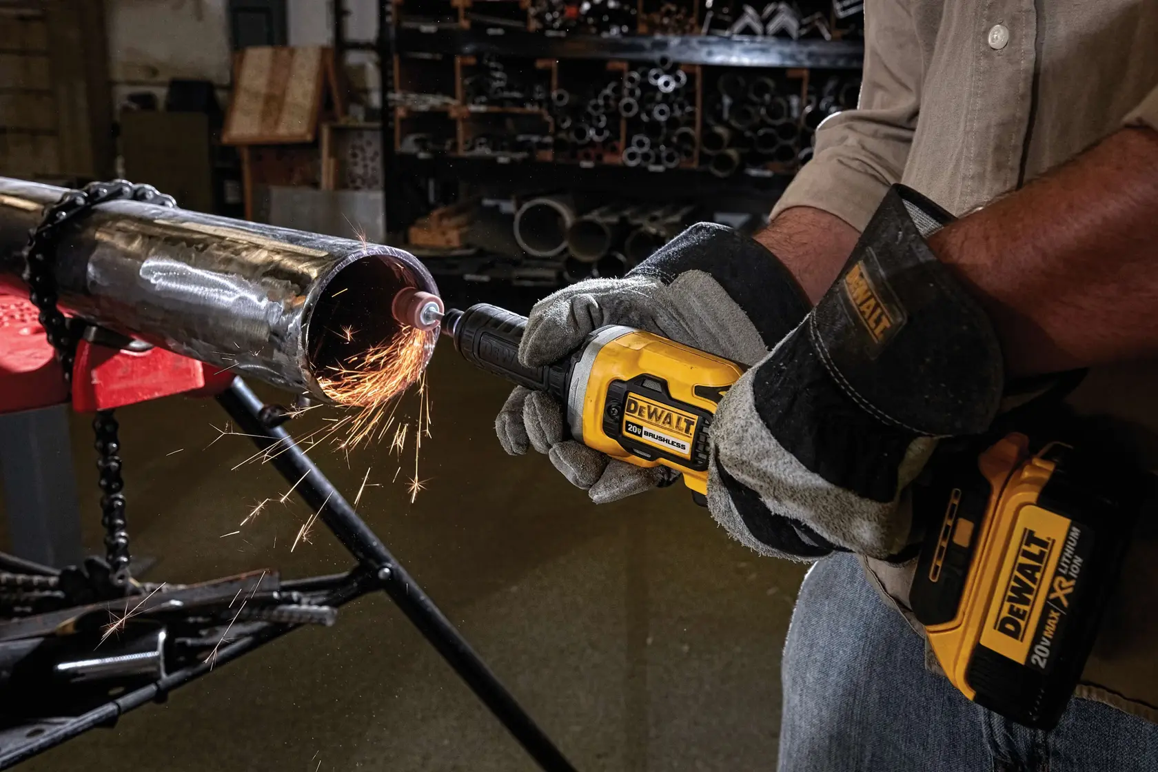 A person wearing protective gloves is using a yellow DEWALT cordless die grinder to grind the edge of a metal pipe, producing sparks in a workshop setting.