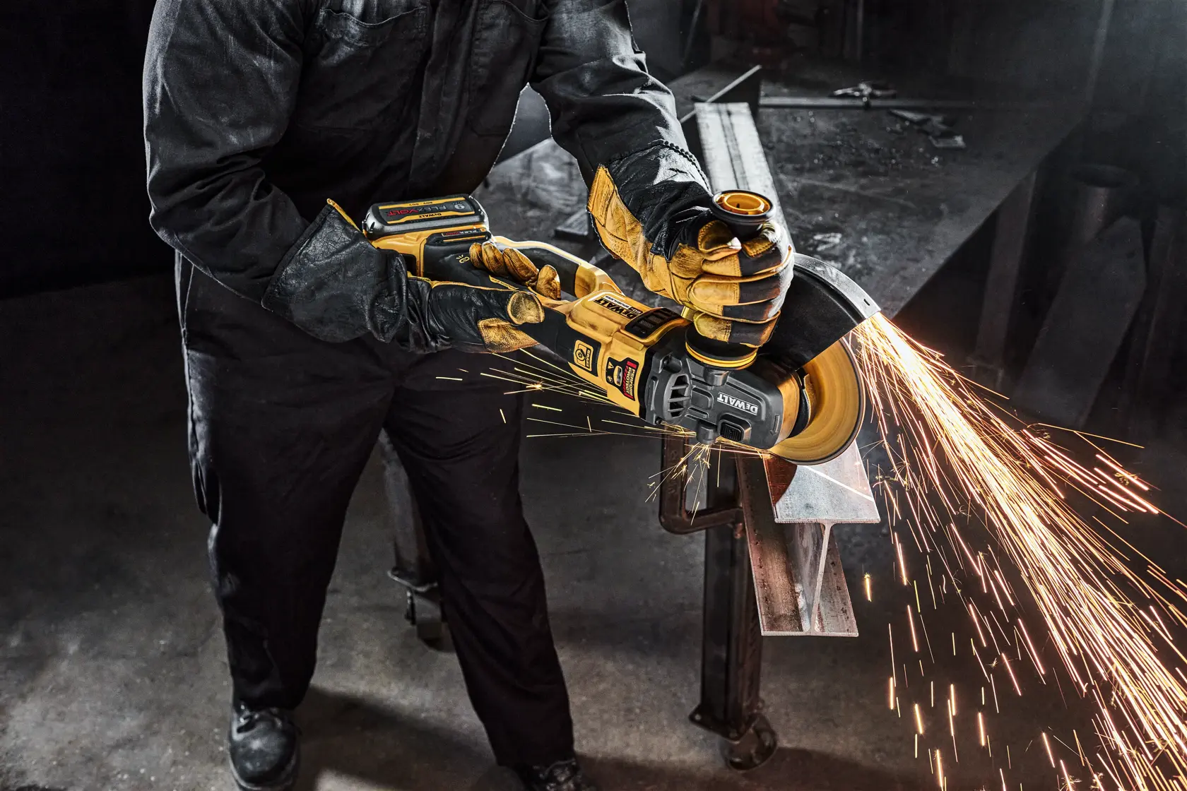 Person wearing protective clothing and gloves using a DEWALT cordless angle grinder to cut a metal bar, generating bright sparks.