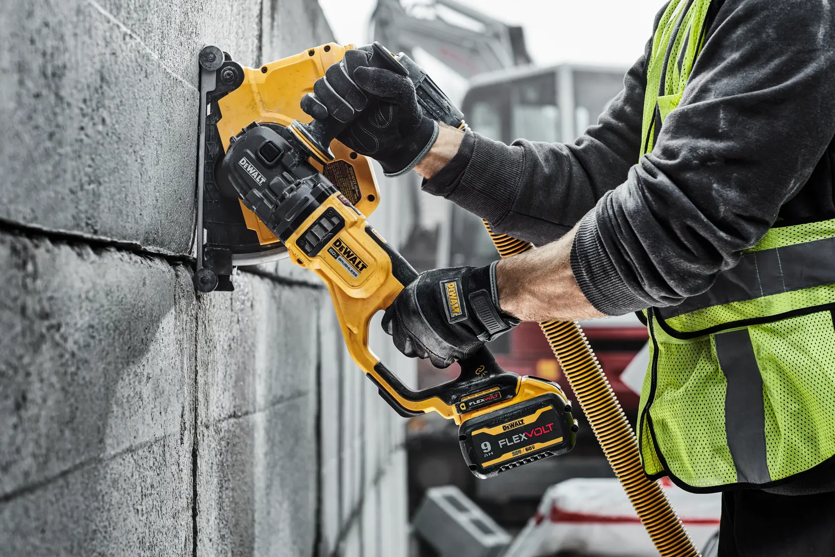 A person wearing gloves uses a DEWALT cordless concrete grinder on a construction site floor. The tool is yellow and black, with a battery pack labeled FLEXVOLT. The setting appears to be an unfinished building.