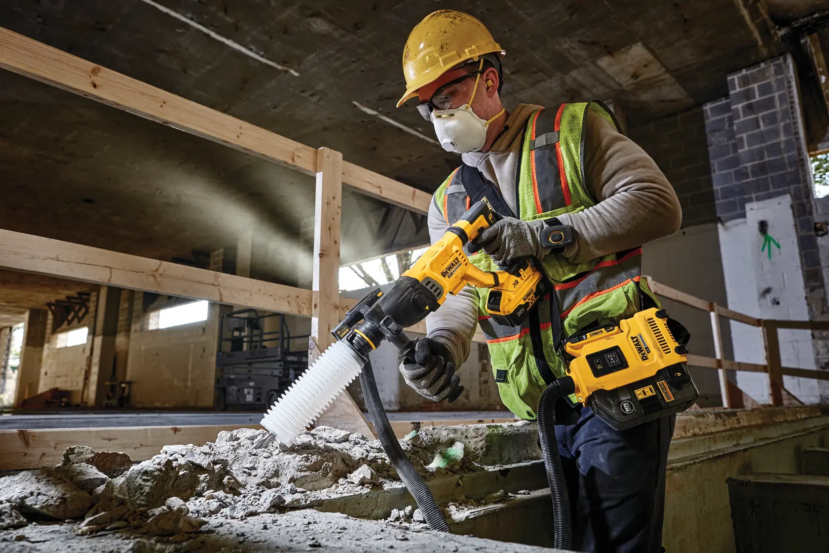 A construction worker using a DEWALT cordless rotary hammer with dust extraction system at a building site. The worker is wearing protective gear, including a helmet, gloves, and safety vest.