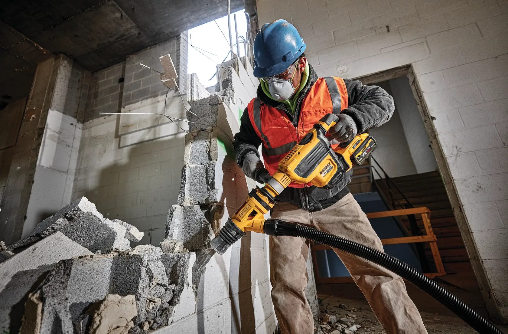 Worker uses DEWALT demolition hammer to break concrete wall in construction site.
