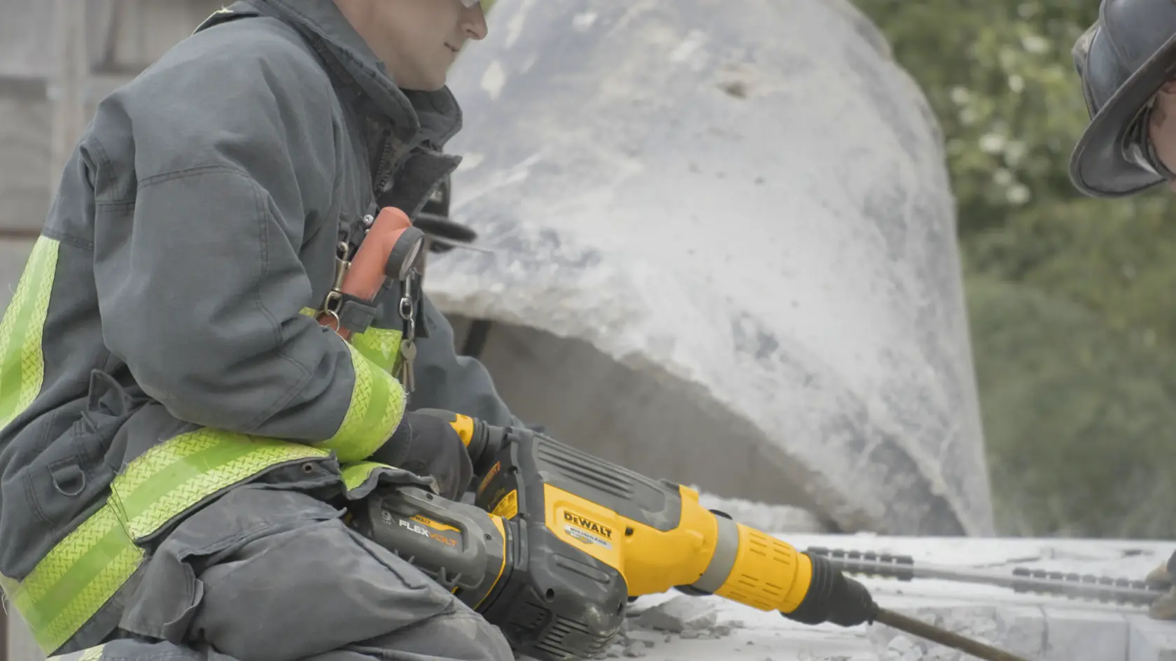 A worker in safety gear uses a yellow DEWALT DCH775X2 power tool for drilling into concrete at a construction site.