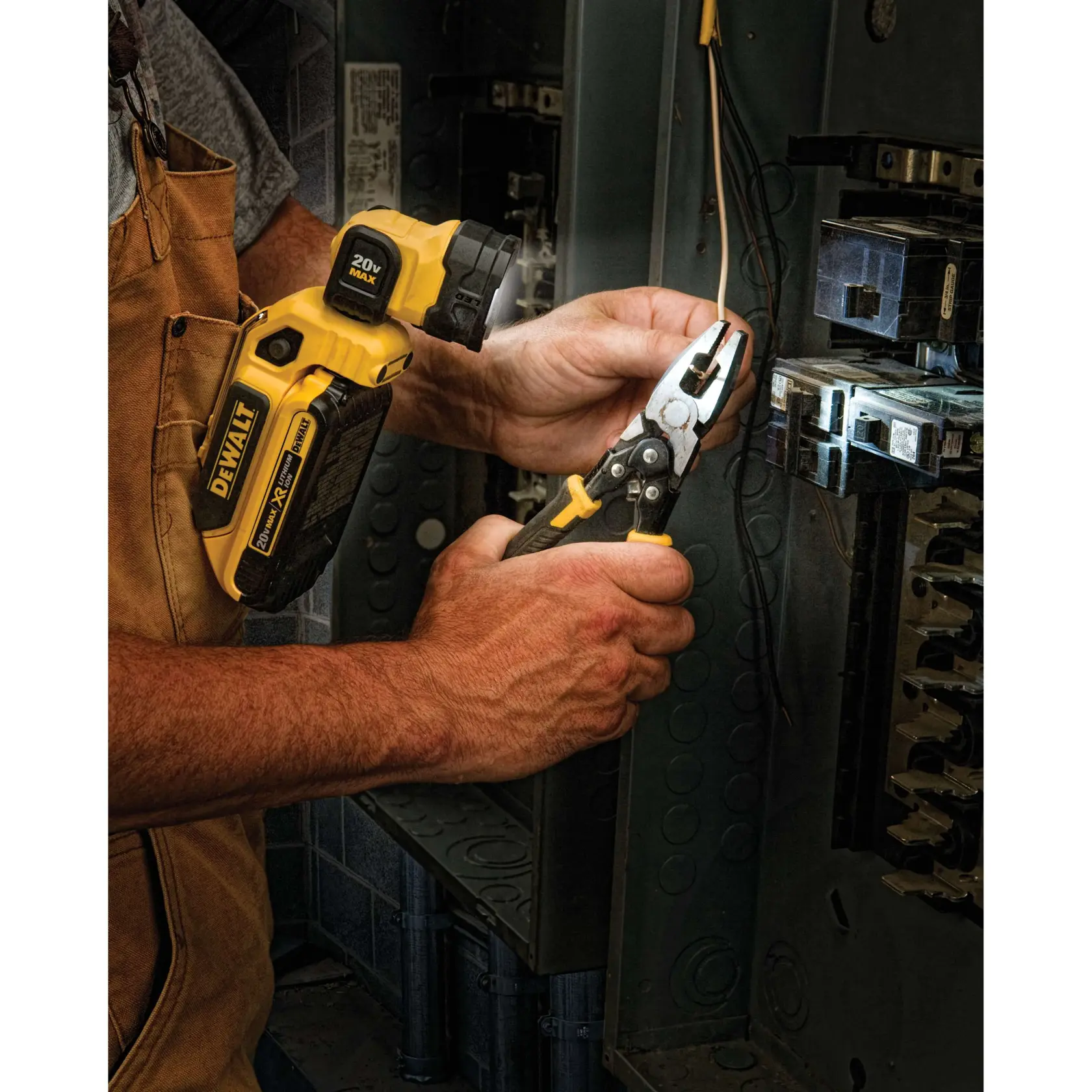 A person using a DEWALT DCL044 20V MAX LED flashlight to illuminate an electrical panel while working with pliers on wires.