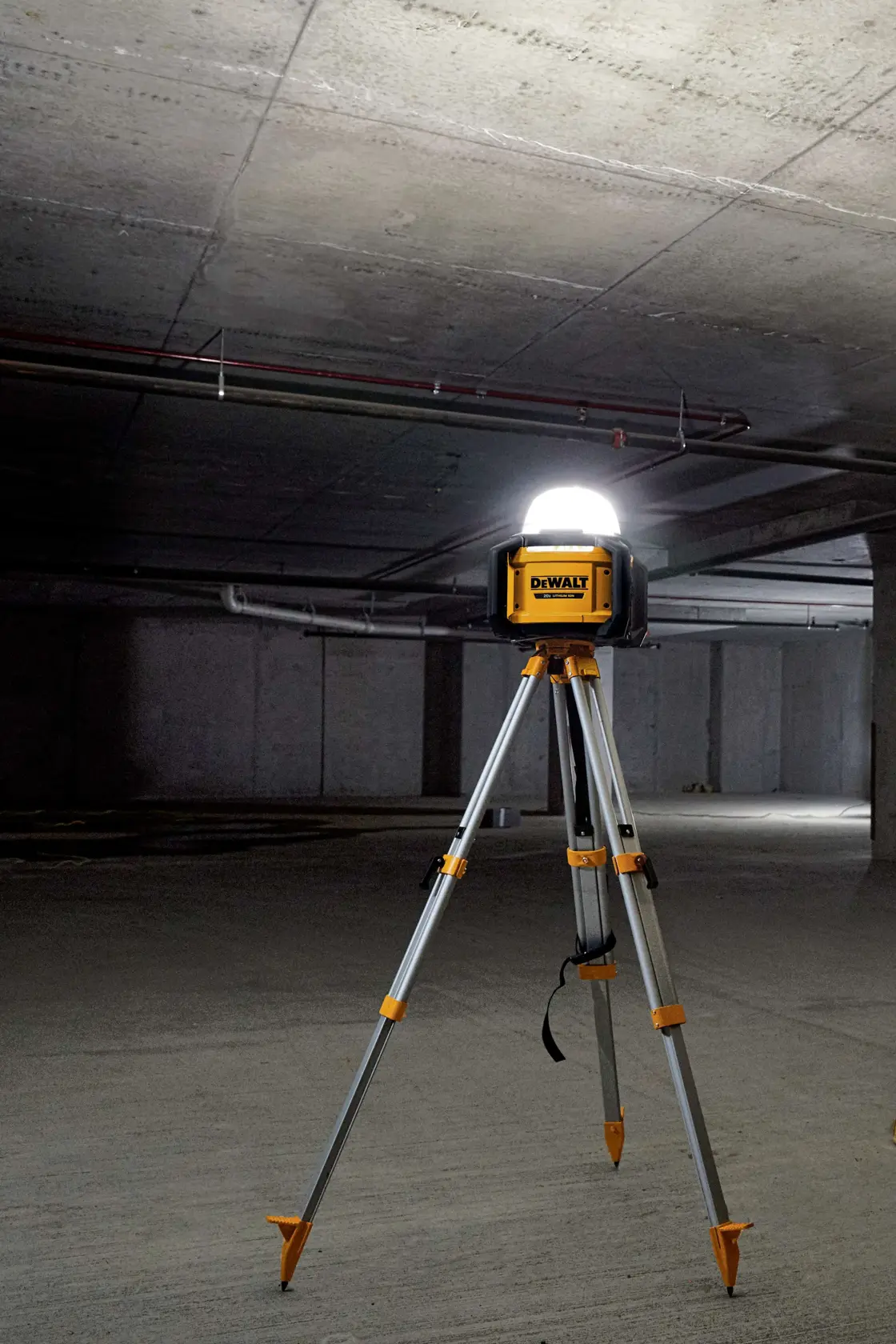 A DEWALT portable work light on a tripod stand, illuminating a large, empty concrete room or basement.