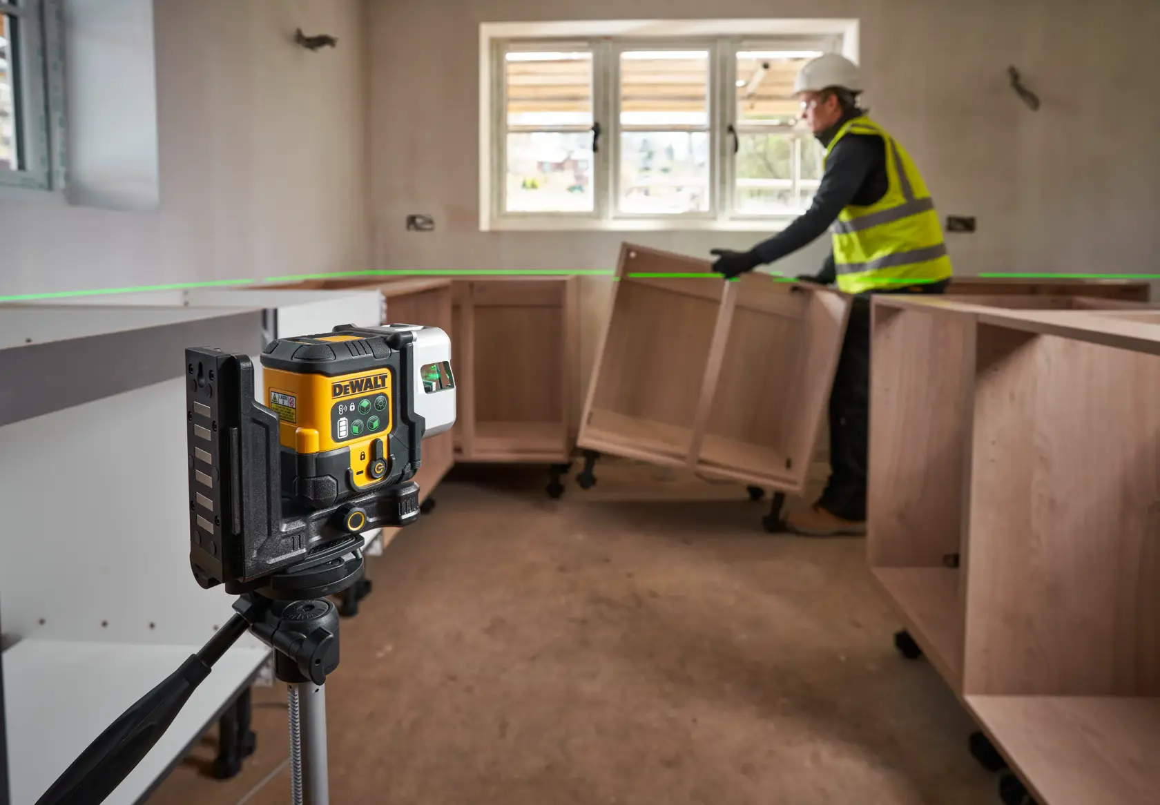 DEWALT laser level on a tripod projecting a green line in a room where cabinets are being installed.