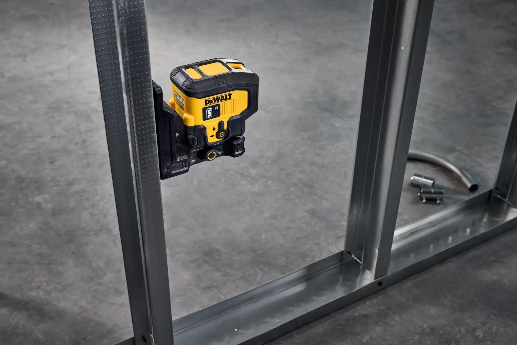 A DEWALT laser level tool mounted on a metal stud frame, used for accurate alignment and leveling during construction work. The tool is yellow and black and is fixed to a vertical metal support with a gray concrete floor in the background.