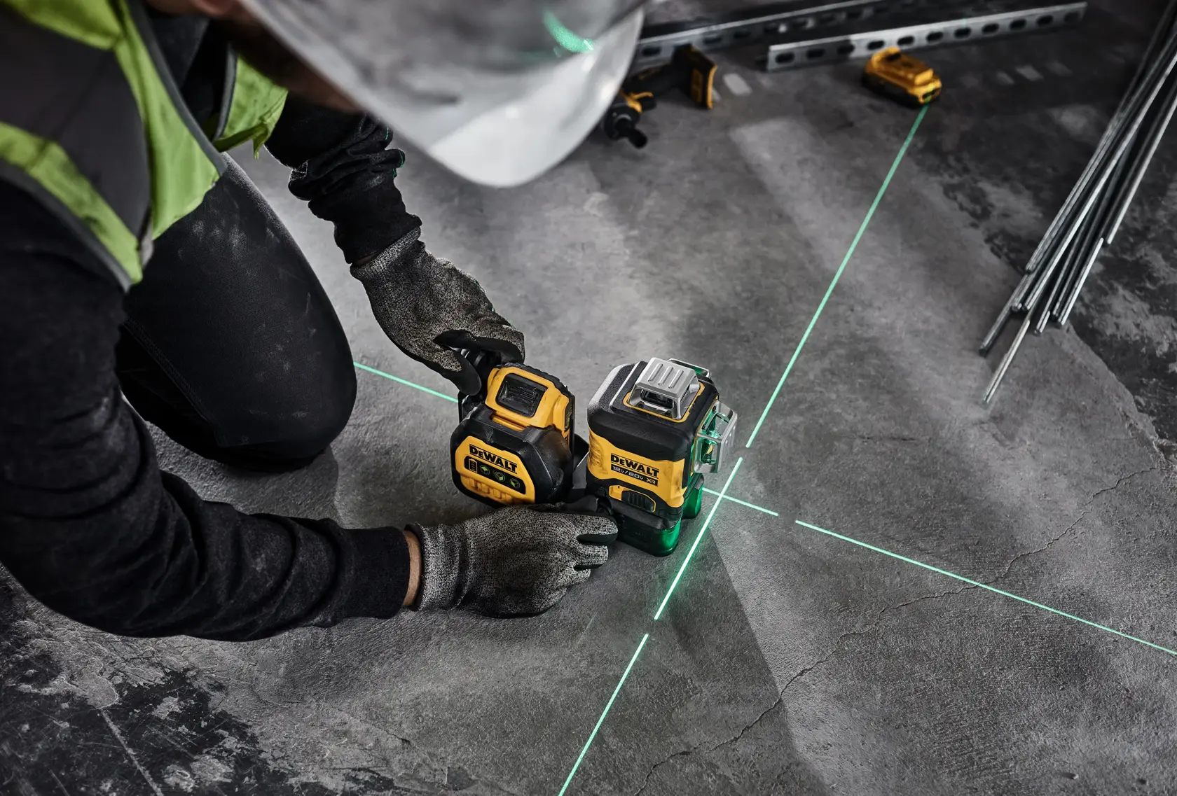 A person wearing gloves and a hard hat is using a DEWALT self-leveling laser level tool on a concrete floor. The tool emits green laser lines, marking precise alignment for construction or layout work.