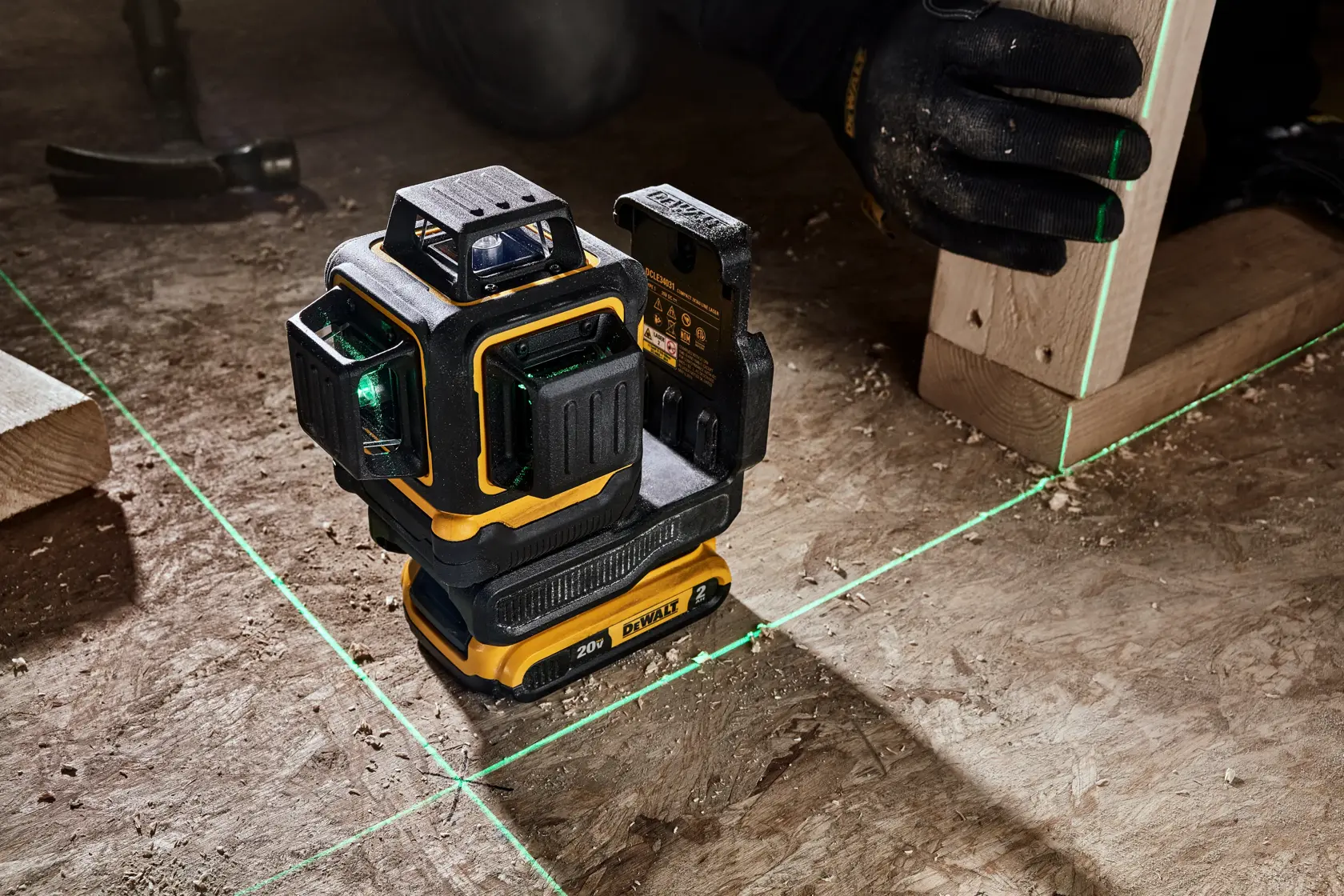 A DEWALT 20V laser level tool projecting green laser lines on a construction site floor, with a worker using the device to align wooden boards.