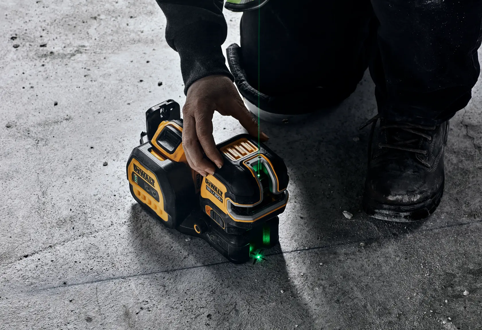 A person using a DEWALT green line laser level on a concrete floor. The tool projects a visible green laser line for accurate alignment in construction or measuring tasks.