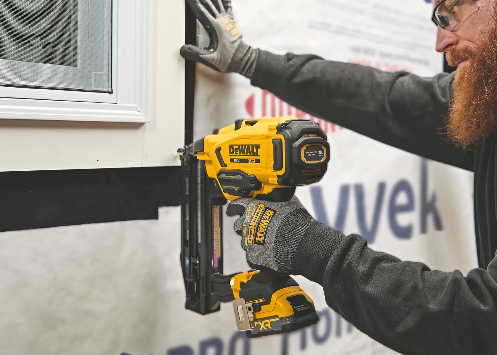 Une main tenant une agrafeuse sans fil DEWALT jaune et noire, utilisée pour fixer une plinthe dans un coin sur un sol de couleur claire.