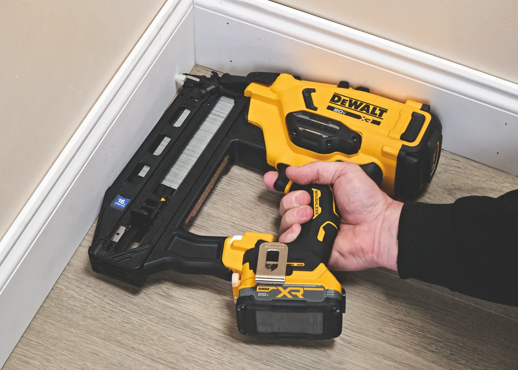 Une personne utilise un pistolet à clous sans fil DEWALT 20V pour fixer une moulure au mur près du plafond.