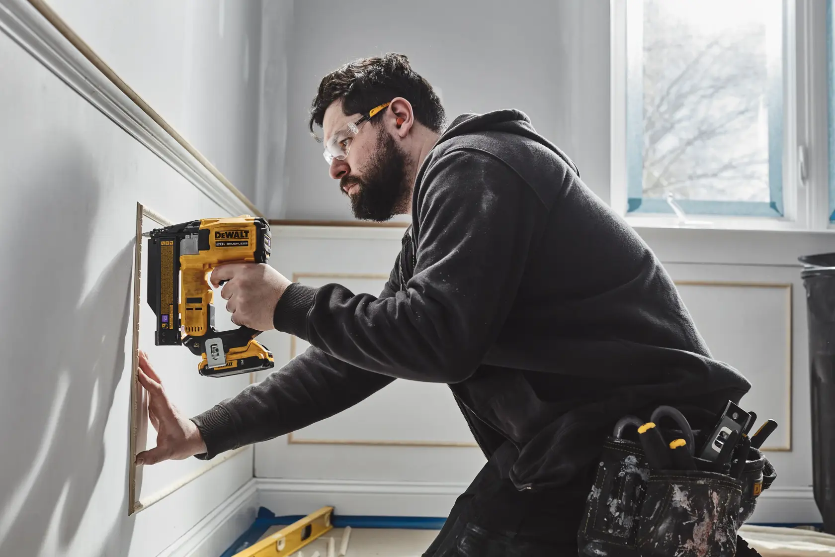 A person uses a DEWALT 20V brushless cordless tool, model DCN623D1, to nail trim onto a cabinet. Text on the image highlights the compact size of the tool with measurements of 8.30 inches wide and 9.20 inches tall.