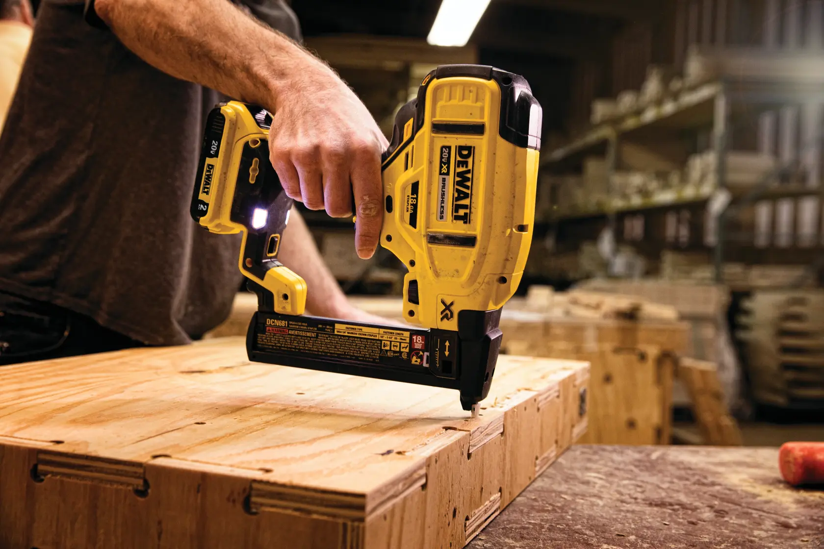 A person is using a DEWALT DCN681B cordless nailer to fasten wooden planks in a workshop setting.