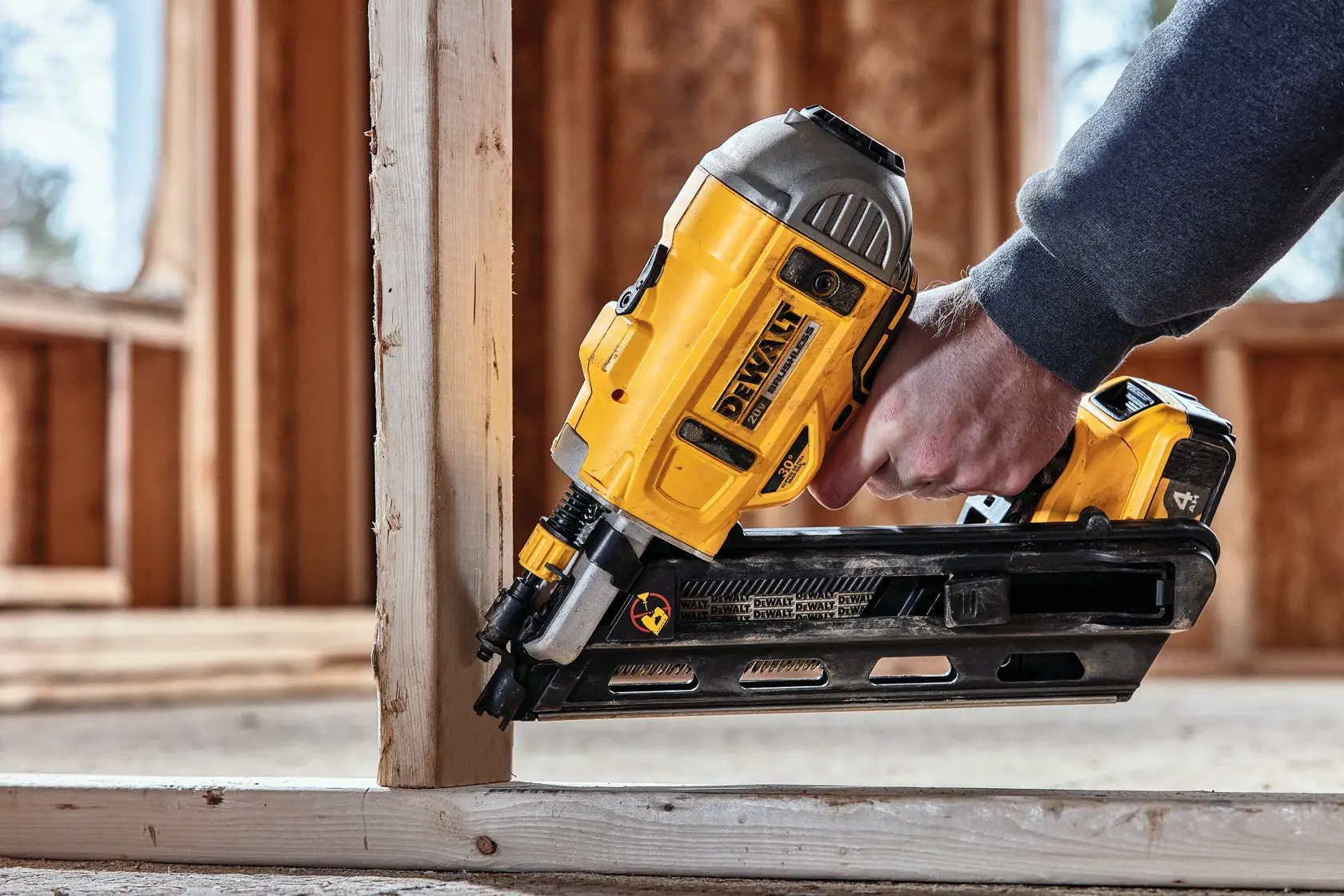 A person uses a DEWALT cordless framing nailer to fasten a wooden beam at a construction site.