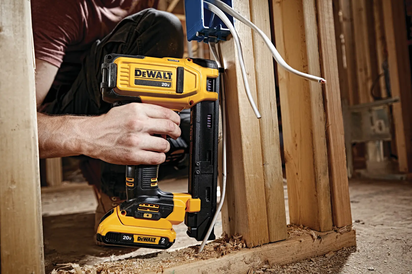 A DEWALT 20V cordless cable stapler being used to secure electrical wires to wooden framing at a construction site.