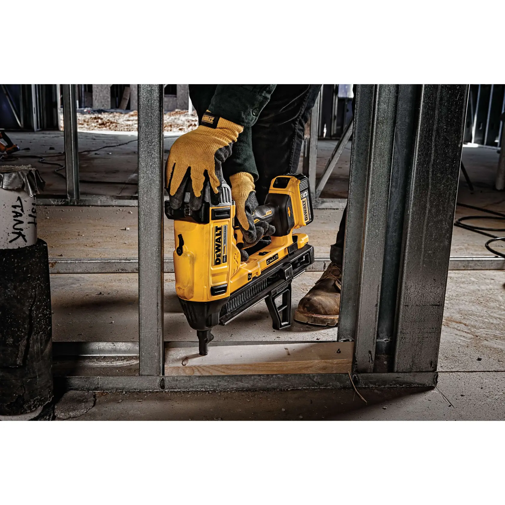 A person wearing gloves is using a yellow DEWALT cordless nail gun to secure a wooden piece to a metal frame in a construction setting.