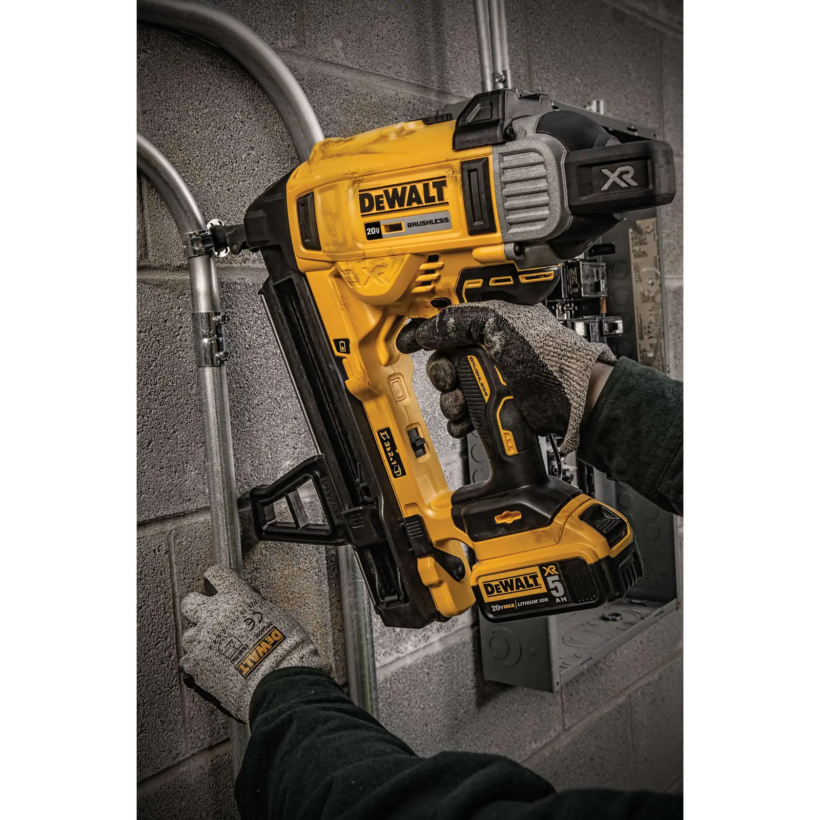 A person wearing gloves is using a DEWALT XR 20V brushless cordless nailer to fasten metal conduit to a concrete wall.