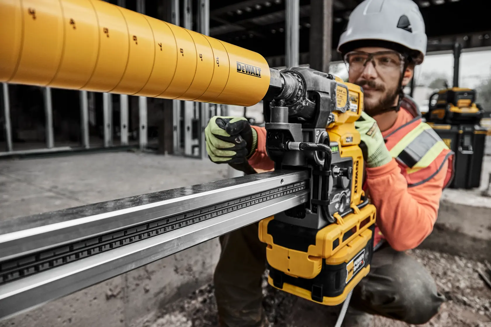 A worker wearing safety gear operates a DEWALT power tool, specifically a yellow cordless rail saw, at a construction site. The worker's face is blurred for privacy.