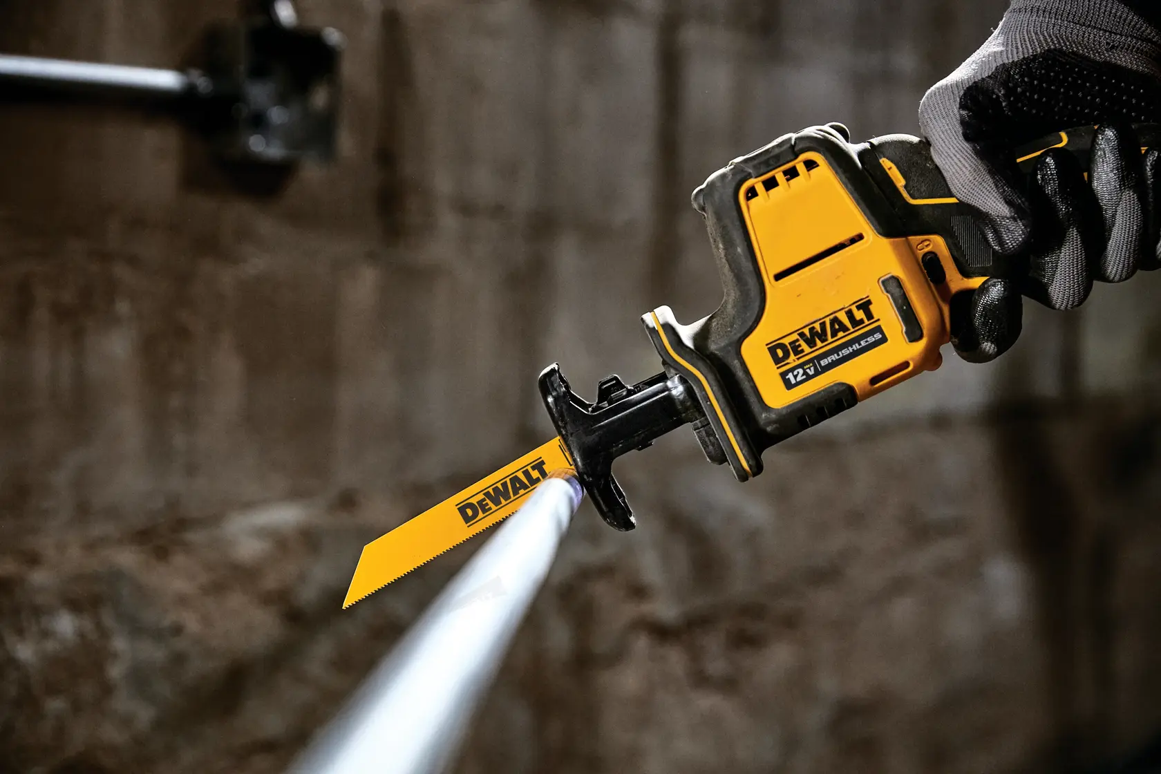 A close-up of a DEWALT 12V cordless reciprocating saw being used to cut a metal pipe. The tool is held in a gloved hand and features a yellow and black design.