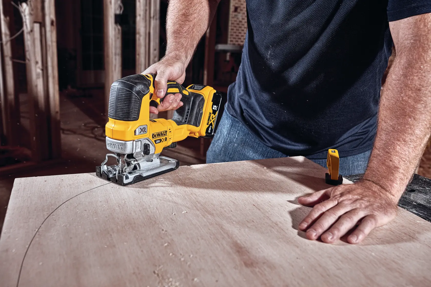 A person using a DEWALT cordless jigsaw (model DCS334B) to cut a curved line into a piece of wood in a workshop setting.