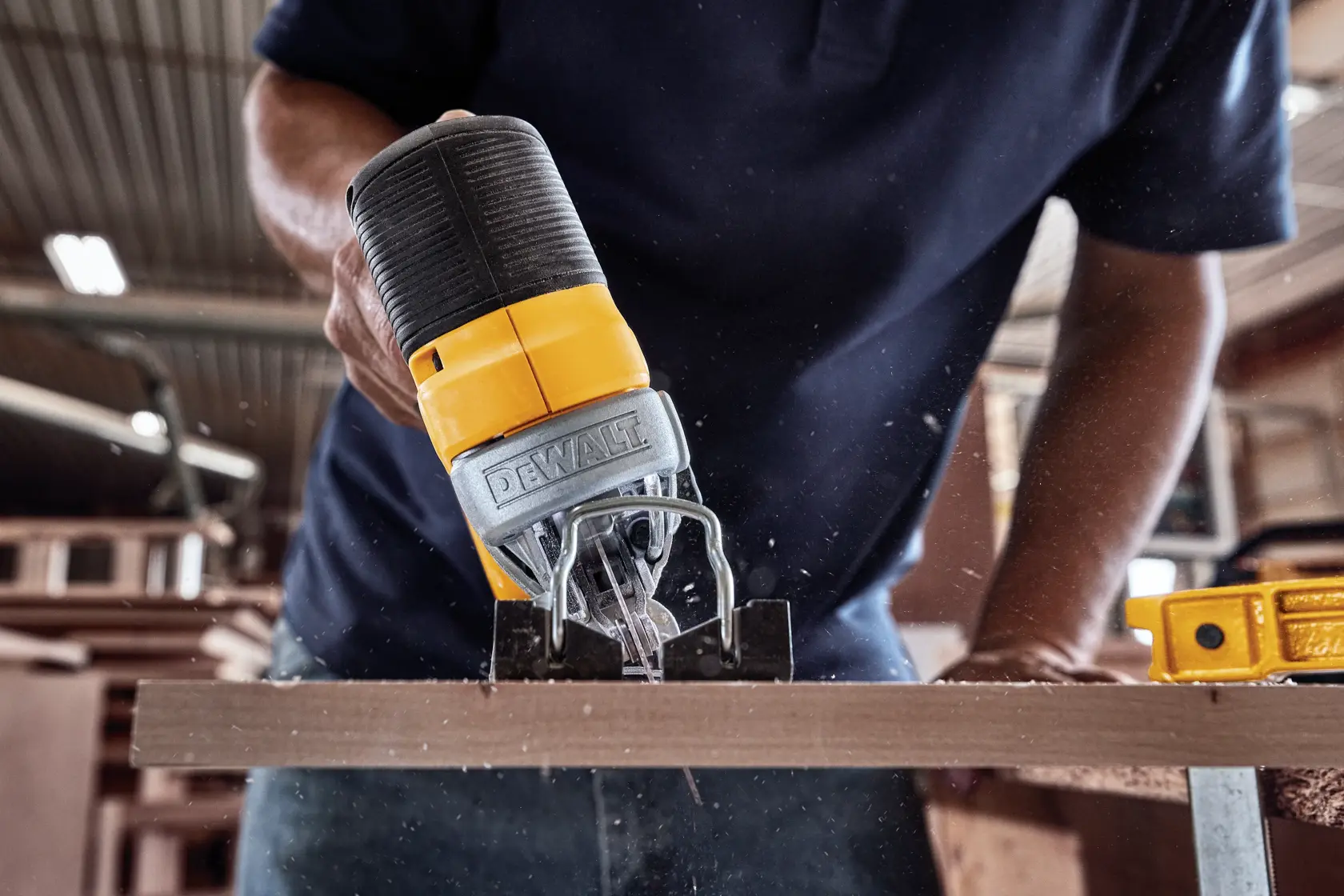 A close-up of a person using a DEWALT cordless jigsaw to cut a piece of wood in a workshop.