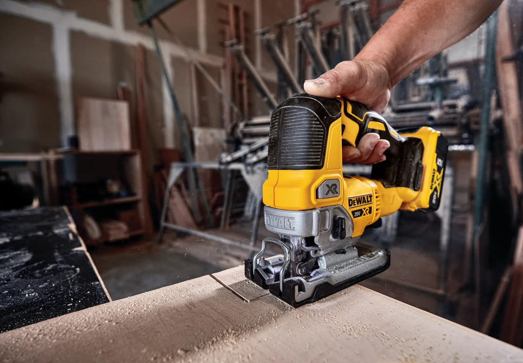 A person using a DEWALT cordless jigsaw to cut wood in a workshop.