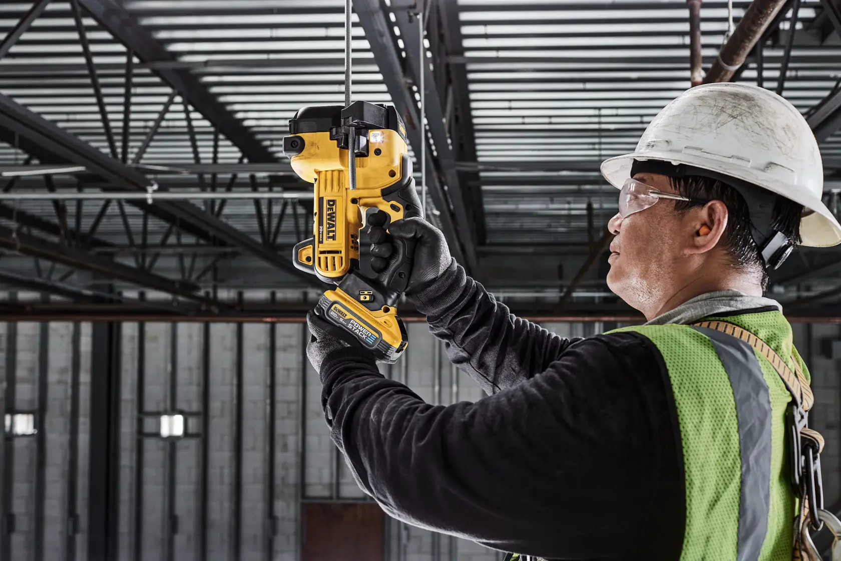 A construction worker wearing a helmet and safety vest uses a DEWALT DCS350B tool to cut a metal rod in an industrial setting.