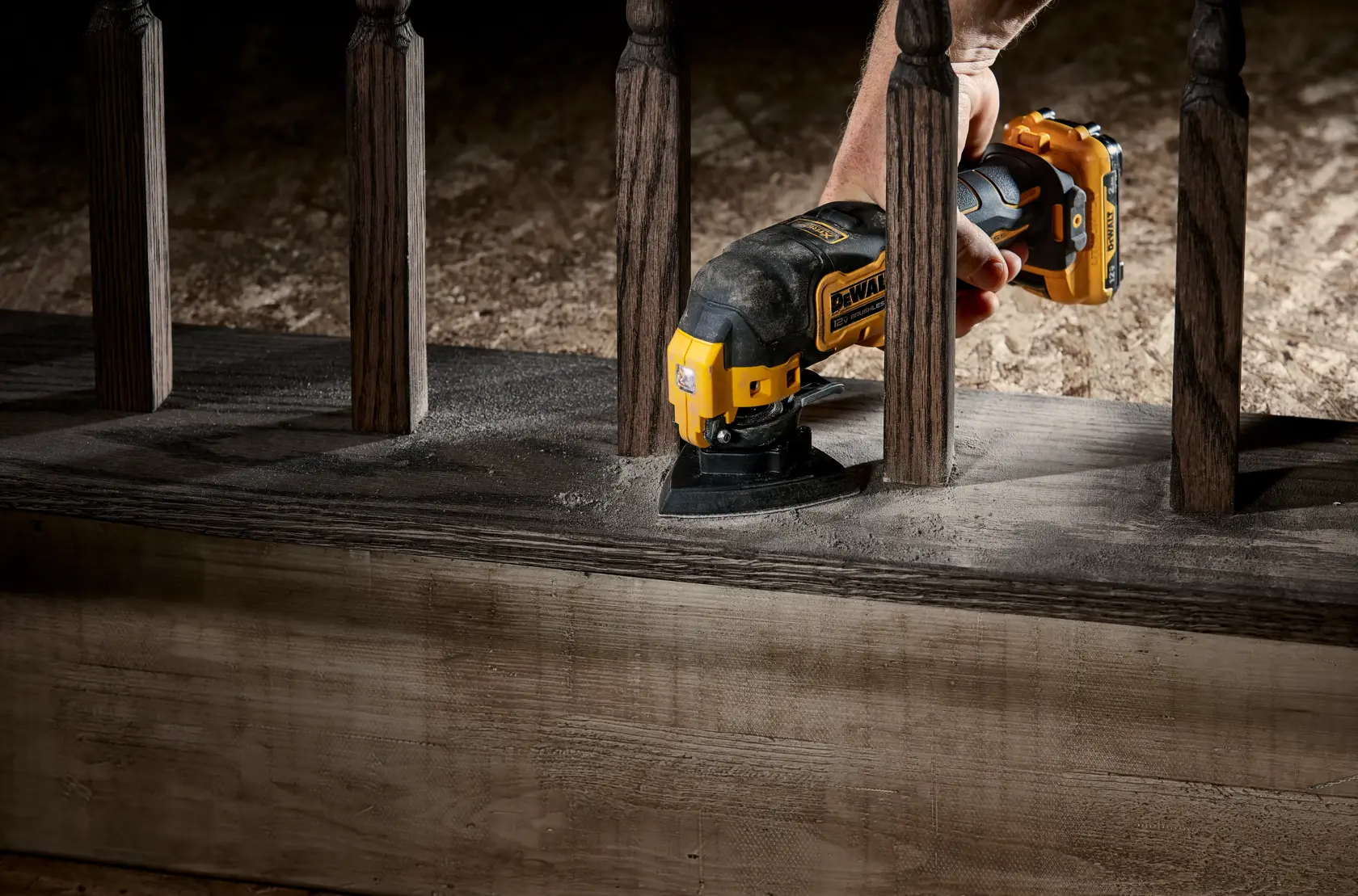 A DEWALT cordless oscillating tool being used to sand wood between railings.